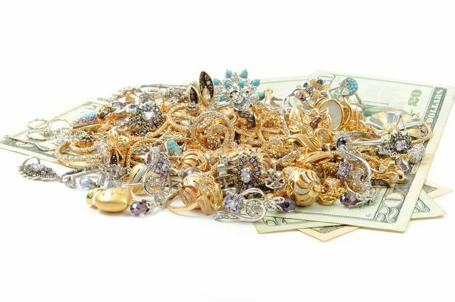 Pile of jewelry of gold, silver, and jewels sitting on top of American dollar bills
